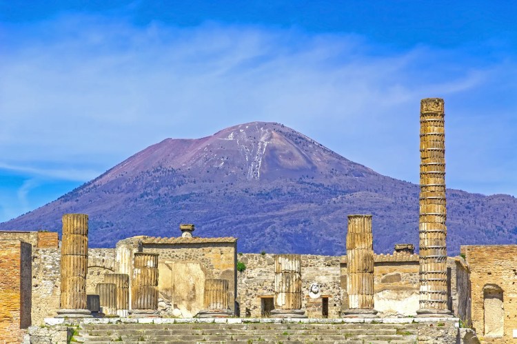 Ruinas de una ciudad antigua con un volcán en segundo plano.